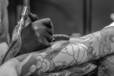 grayscale photo of person applying tattoo